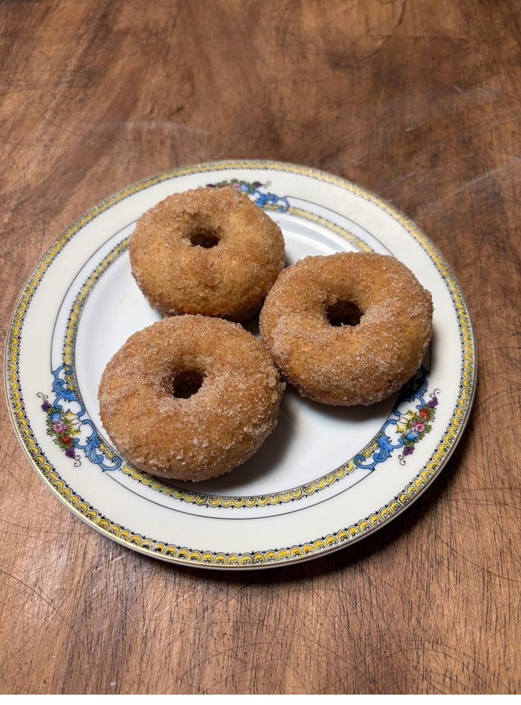 Three cinnamon-sugar apple cider donuts on a floral-rimmed plate on a wooden board.