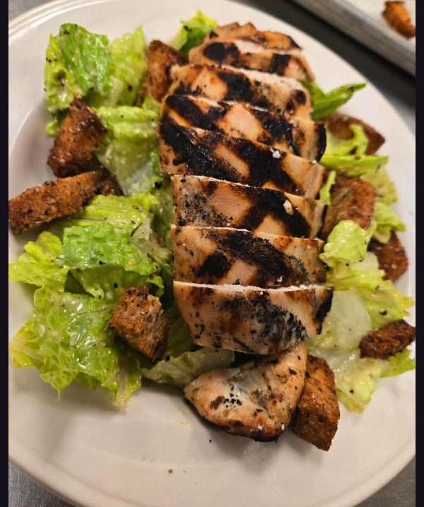 Sliced grilled chicken with dark grill marks fanned over romaine lettuce with croutons and cracked pepper.