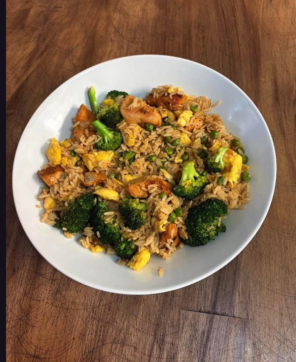A bowl of fried rice with chicken, broccoli florets, peas and scrambled egg.