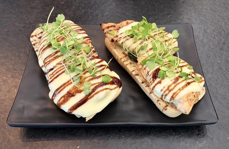 Chicken caprese flatbread on a black plate, covered in melted cheese, striped with balsamic glaze and piled with microgreens.