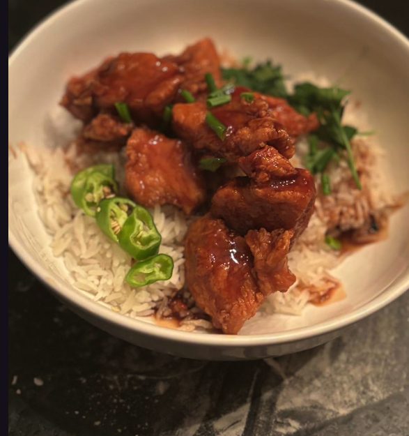 Glazed orange chicken served over white rice in a bowl with sliced green chillies, scallion and cilantro.