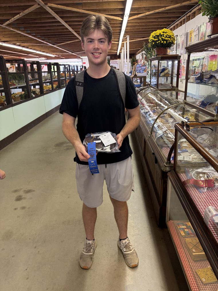 Holding the whoopie pie entry and a blue First Premium ribbon beside the display cases at Deerfield Fair.